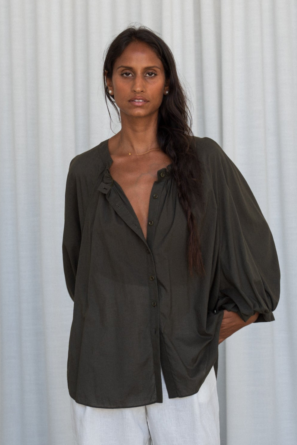 LILLY PILLY woman wearing a khaki Thalia cotton voile shirt blouse showing front view in front of a white curtain background