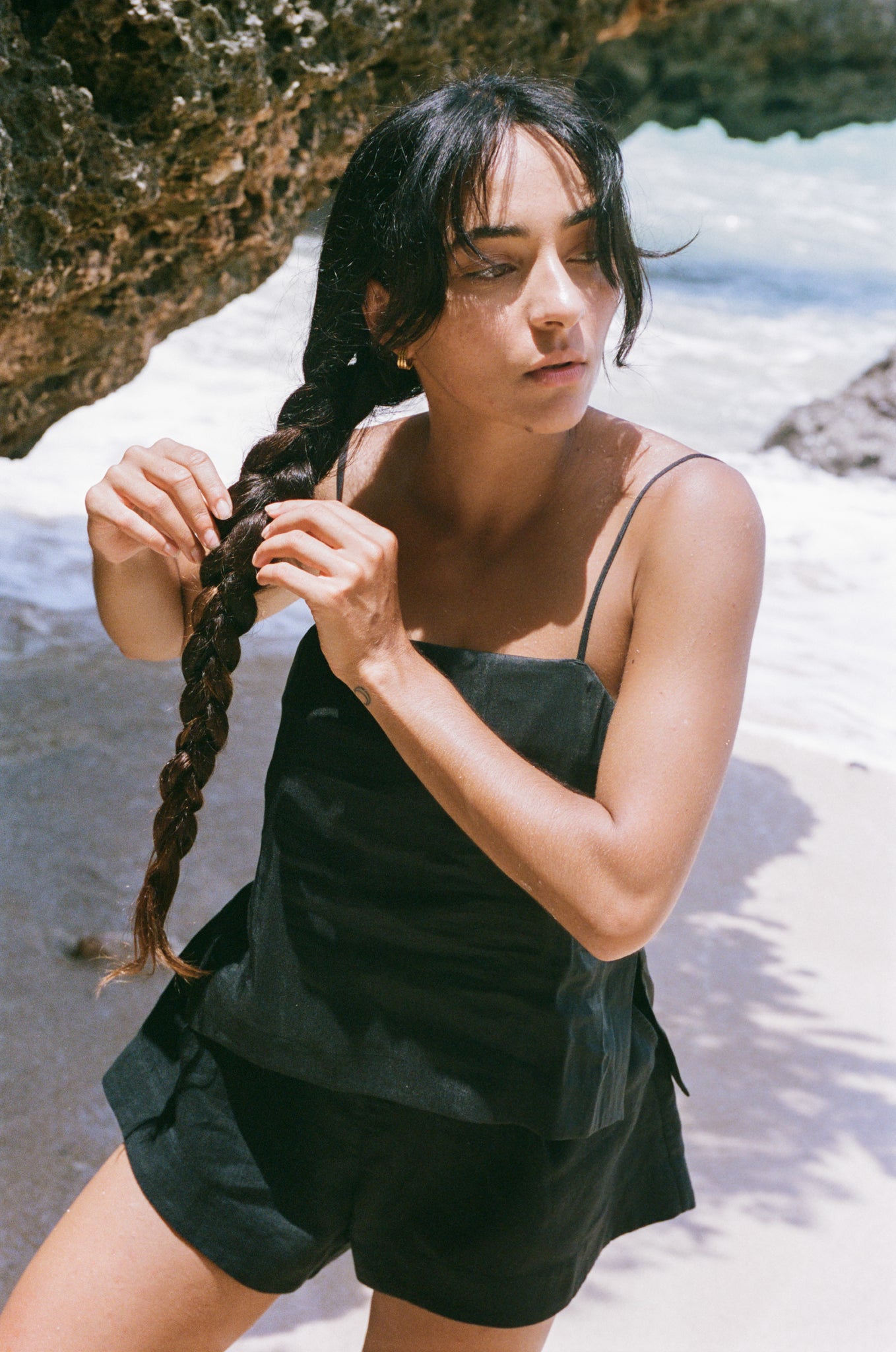 Woman with braided hair standing on a beach wearing Gaia linen shorts