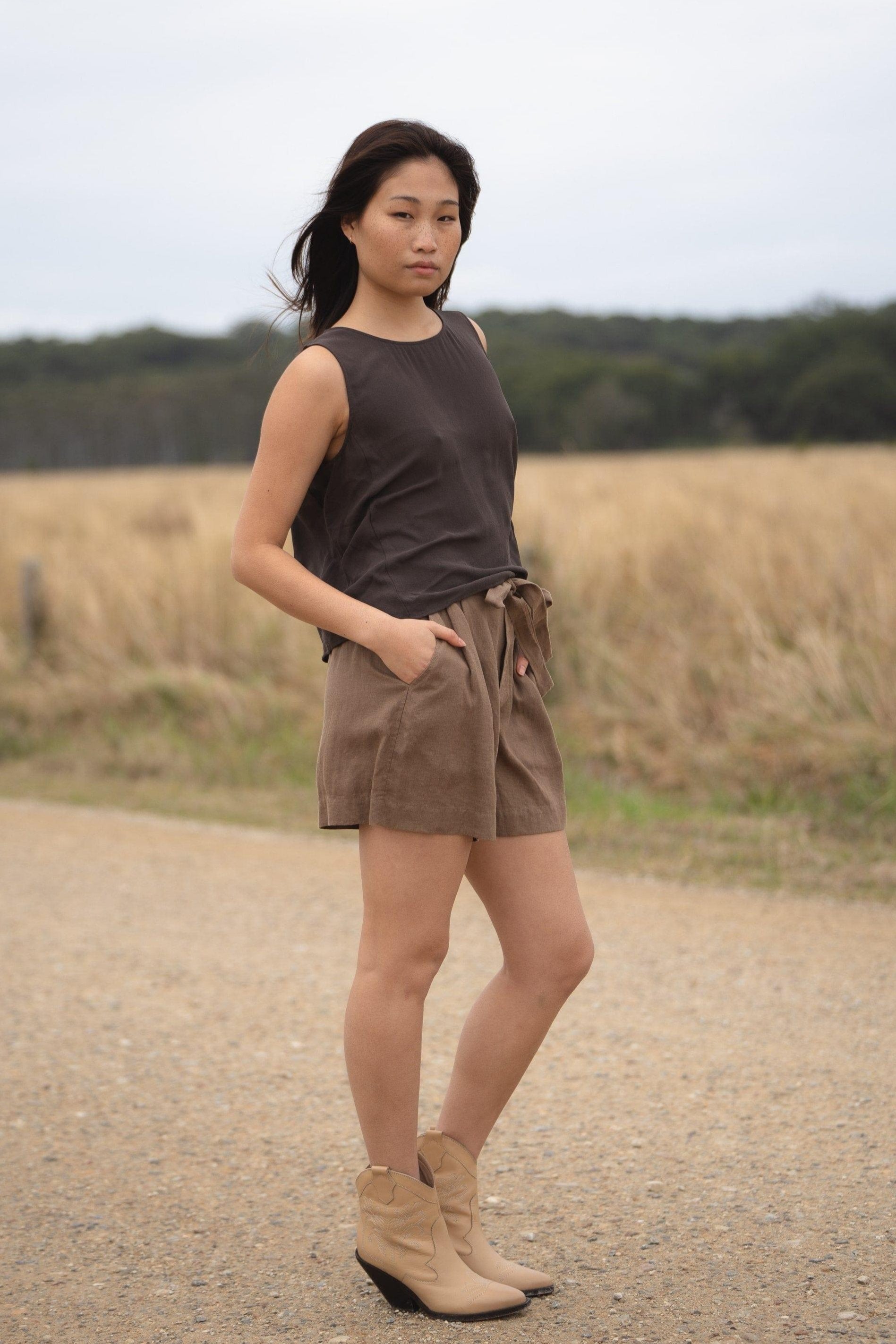 LILLY PILLY girl wearing a brown LULU  silk tank top and DARK  EARTH AMELIA linen shorts, standing on a dirt road