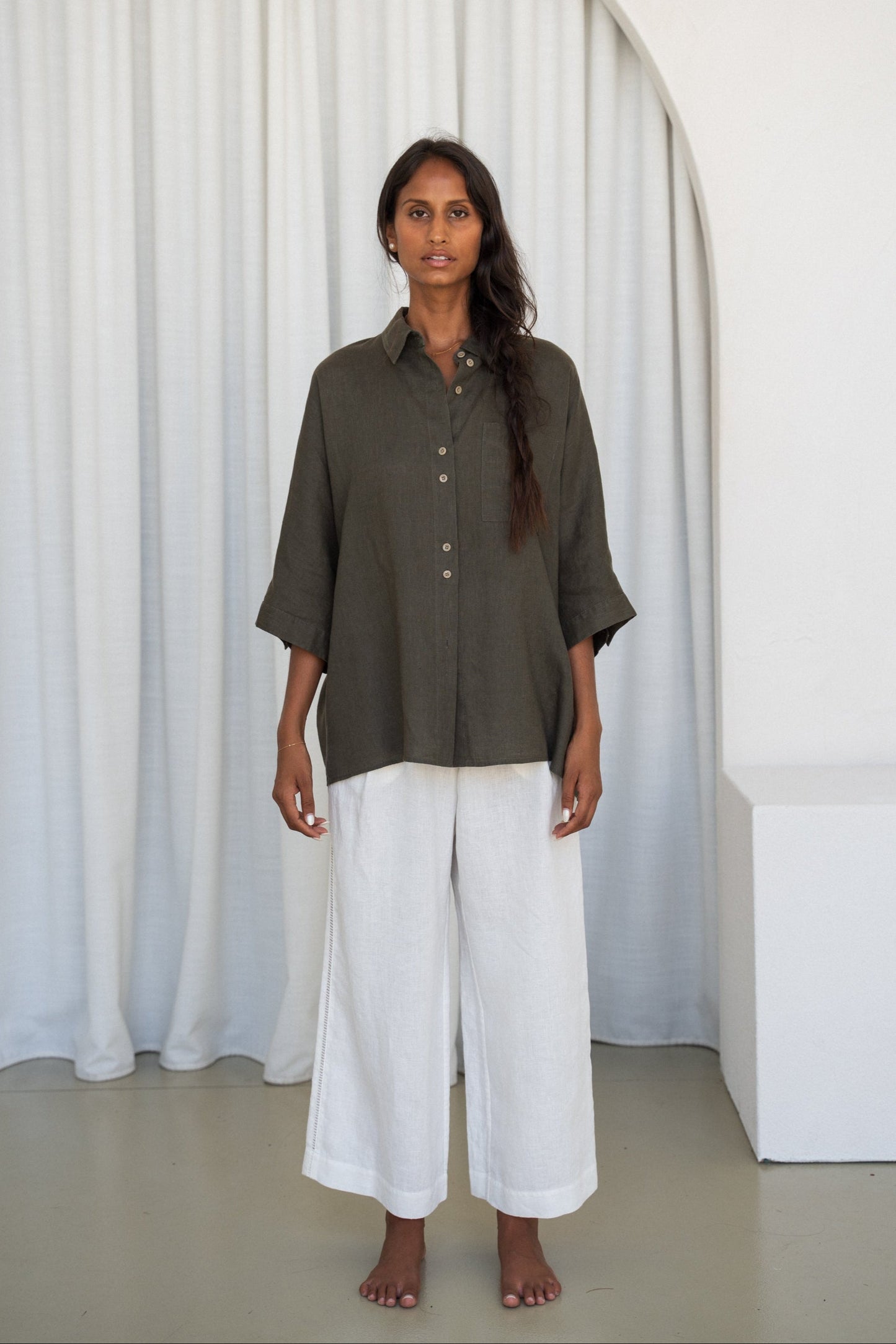LILLY PILLY woman wearing a khaki Pixie linen shirt and Oli white linen pants outfit by an archway