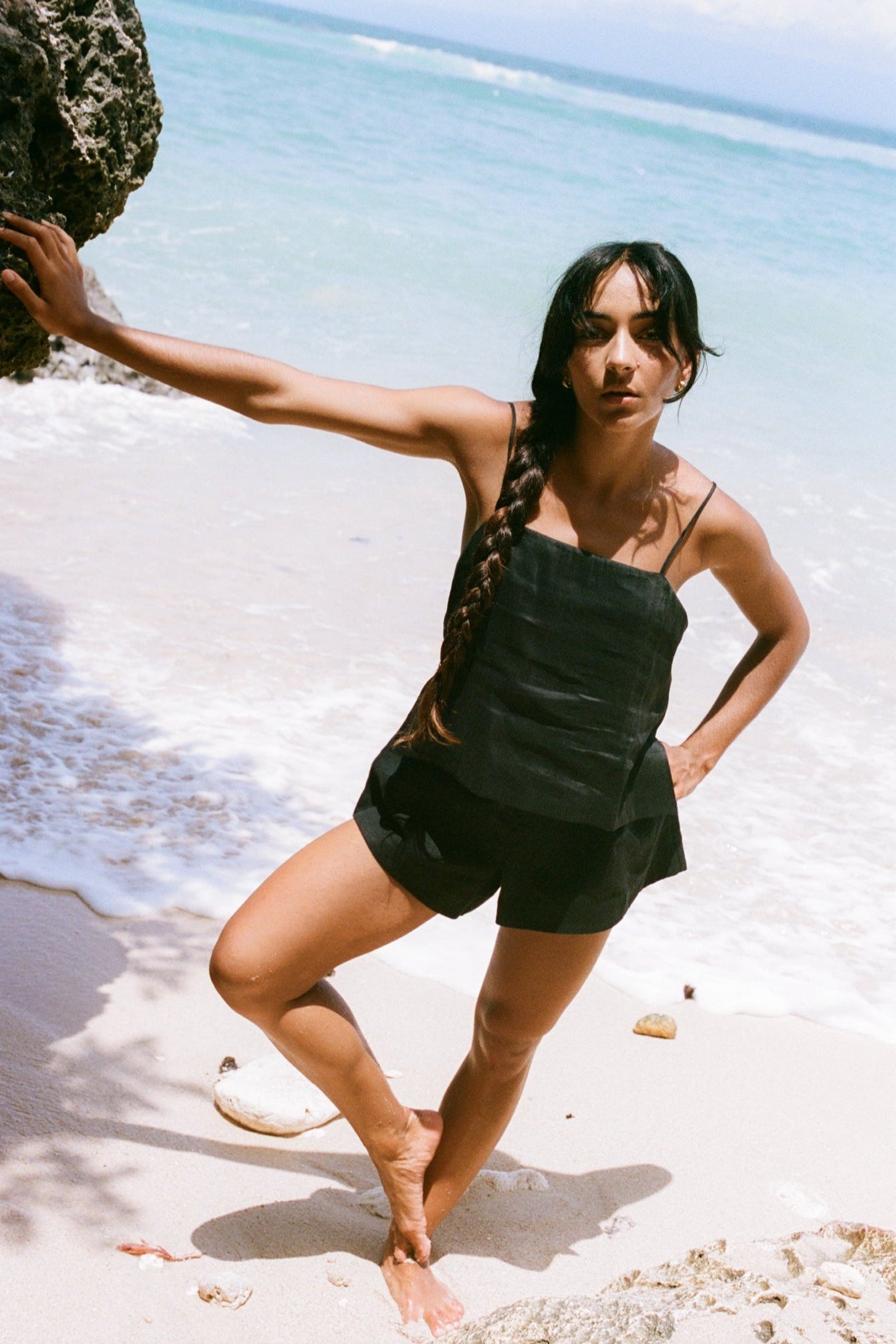 LILLY PILLY woman wearing a black Rosa silk linen cami top and shorts standing on a beach with ocean in the background
