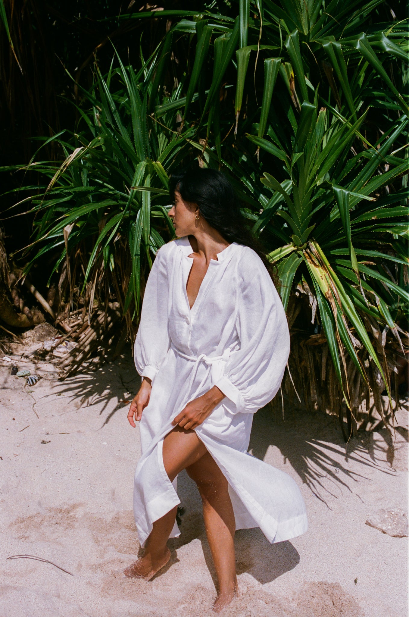 Woman in an ivory Mae linen dress standing in front of green plants