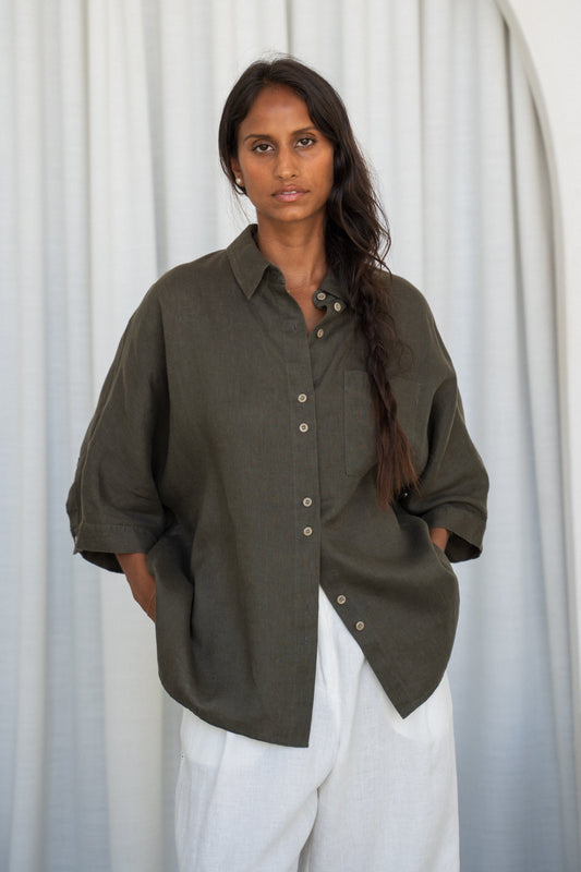LILLY PILLY woman wearing a khaki Pixie linen shirt and Oli white linen pants outfit against a white curtain background